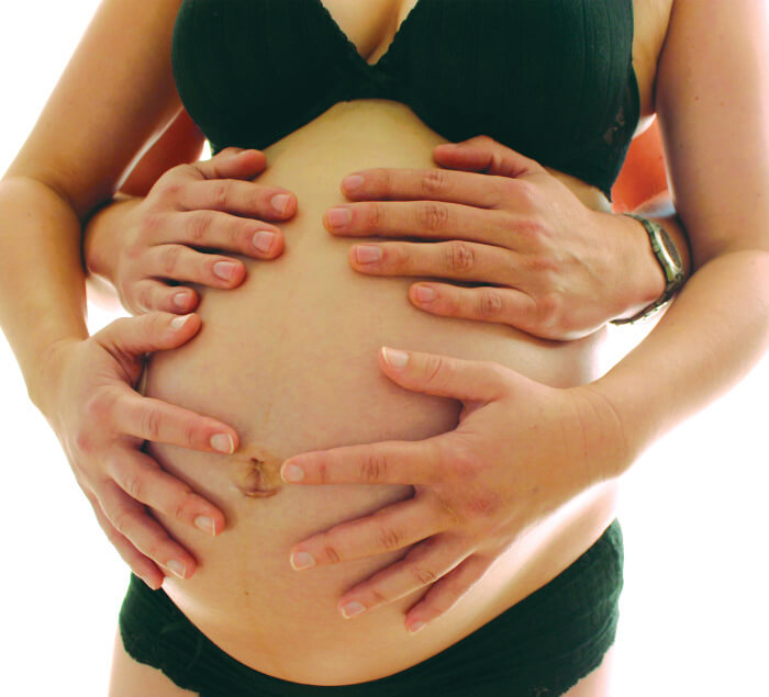Afbeelding man handen op zwangere buik bij artiekl pijnervaring bevalling
