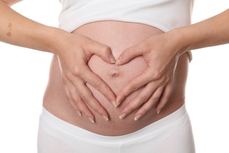 Afbeelding van zwangere buik met twee handen die hartje vormen bij artikel over misselijkheid tijdens zwangerschap